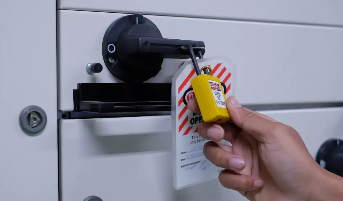 Main installant un cadenas de consignation et une étiquette de danger sur un sectionneur électrique