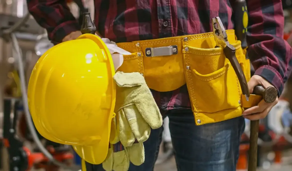 Travailleur tenant un casque de sécurité et des gants, ceinture à outils à la taille