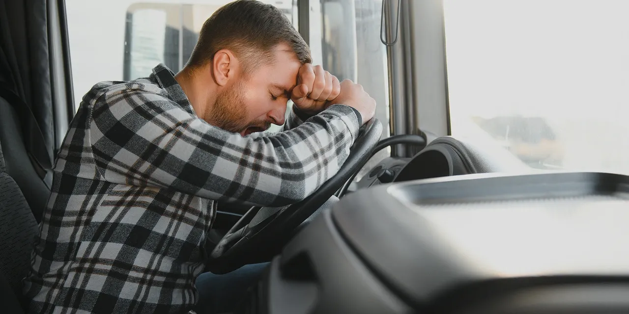 Camionneur fatigué, la tête appuyée sur son poing contre le volant, les yeux fermés