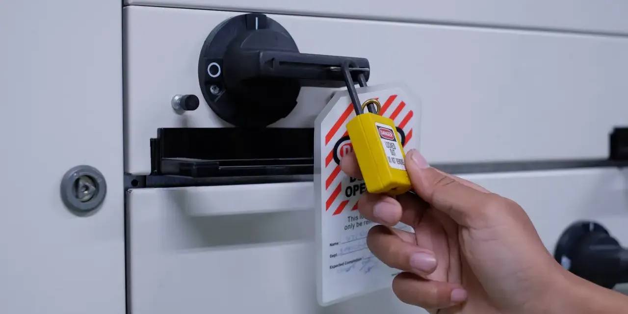 Main installant un cadenas de consignation et une étiquette de danger sur un sectionneur électrique