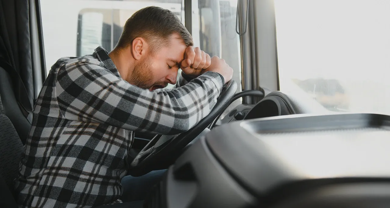 Fatigued commercial truck driver rubbing his eyes at the wheel