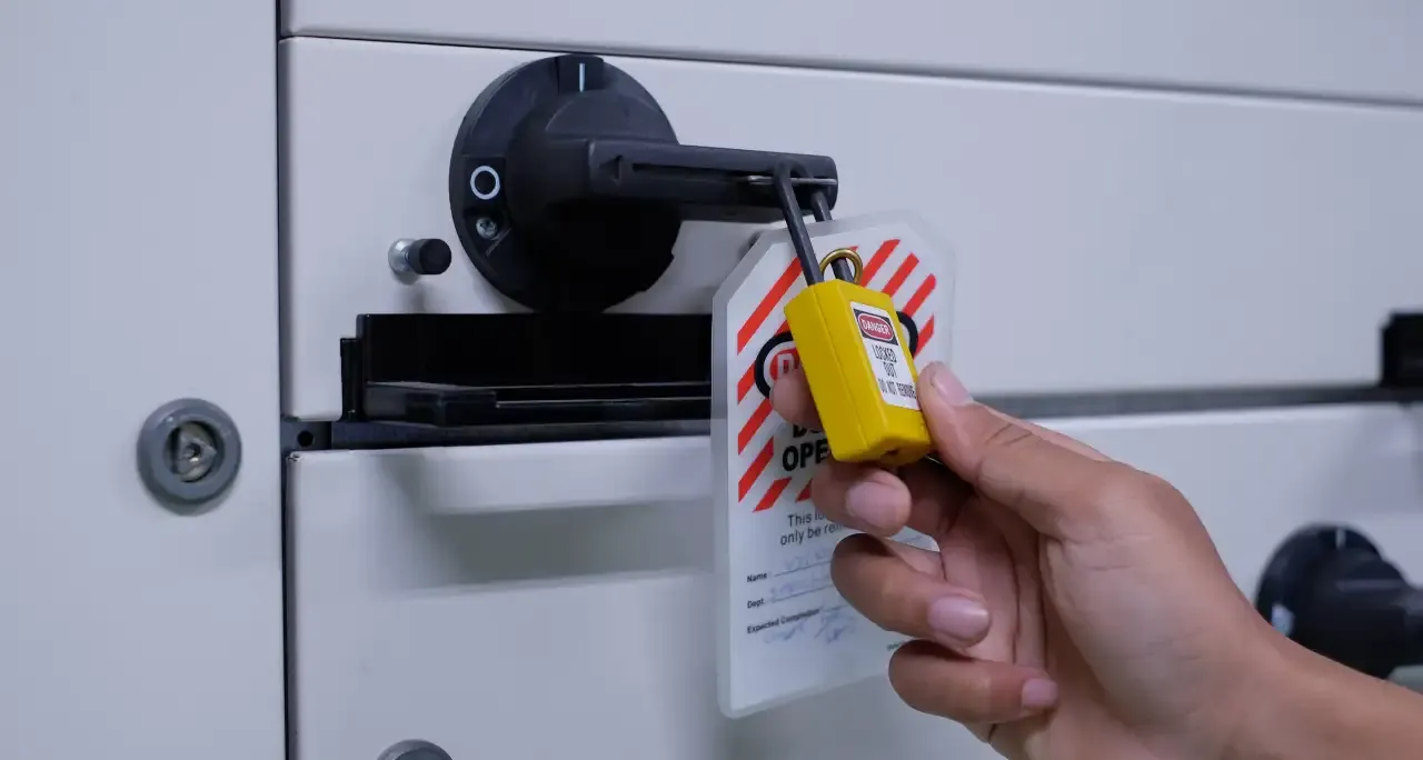 Hand fitting a lockout padlock and danger tag to an electrical disconnect switch