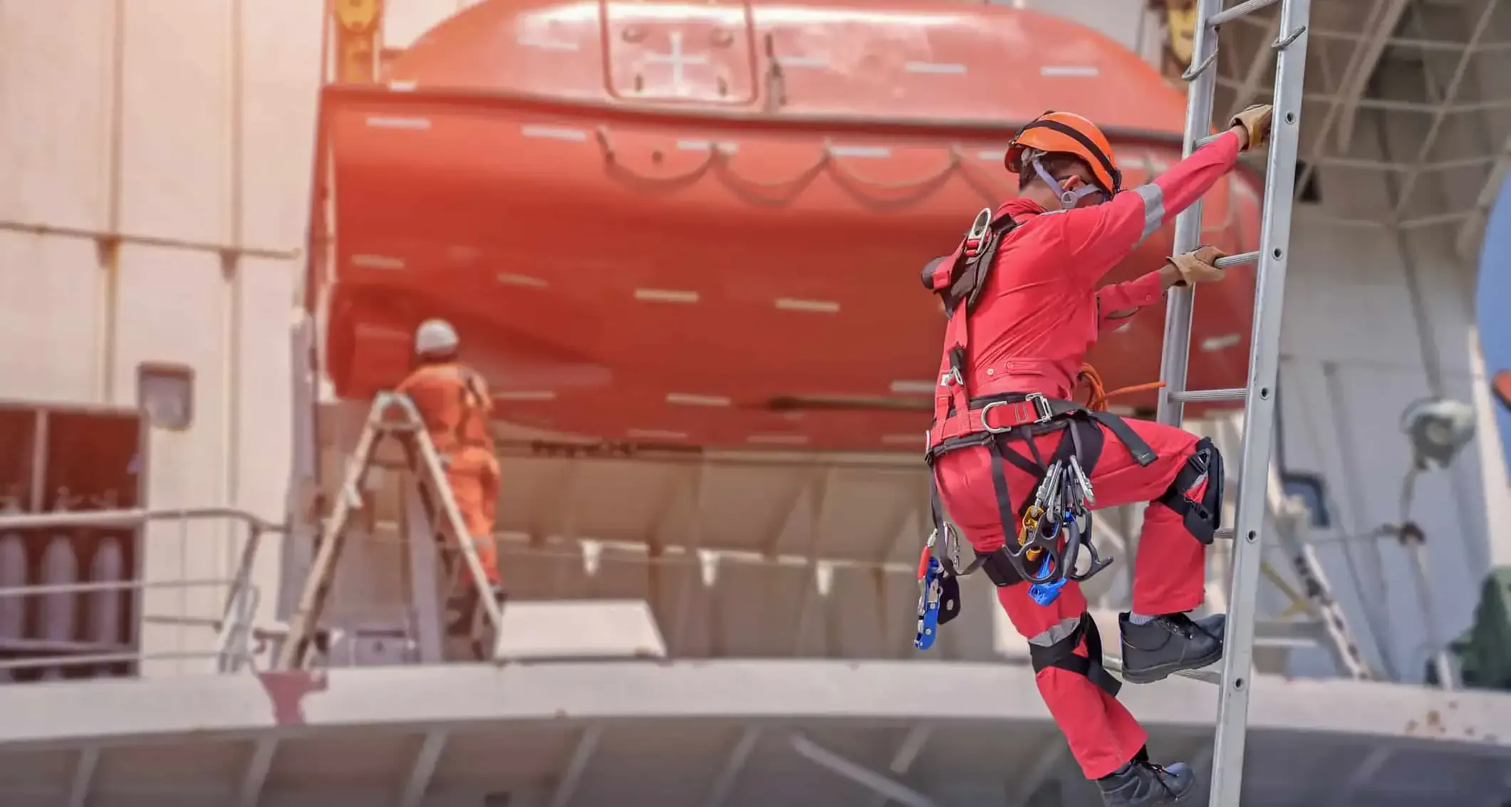 Worker in a hard hat and harness climbing a secured straight ladder