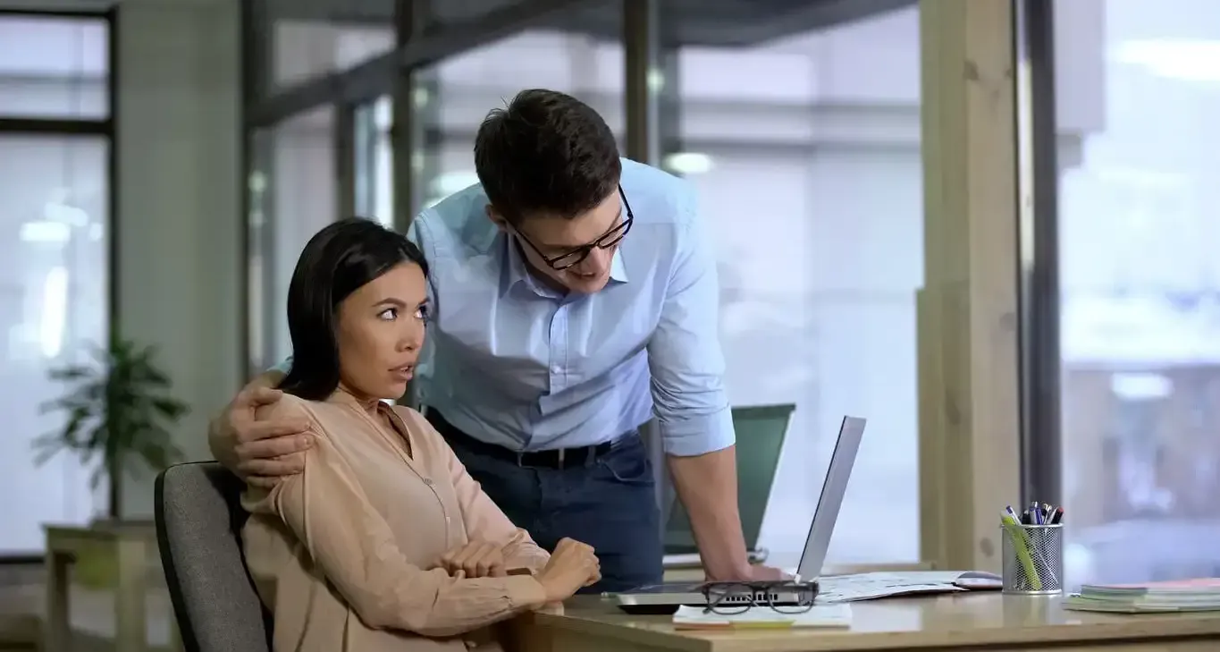 Employee looking uncomfortable as a colleague leans over her workstation