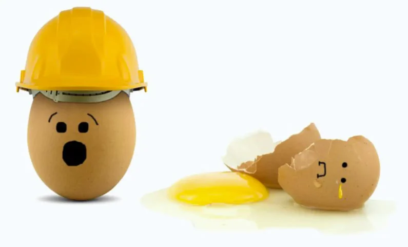 Egg wearing a safety hard hat looking worriedly at another broken egg without a hat, symbolising workplace hazards.